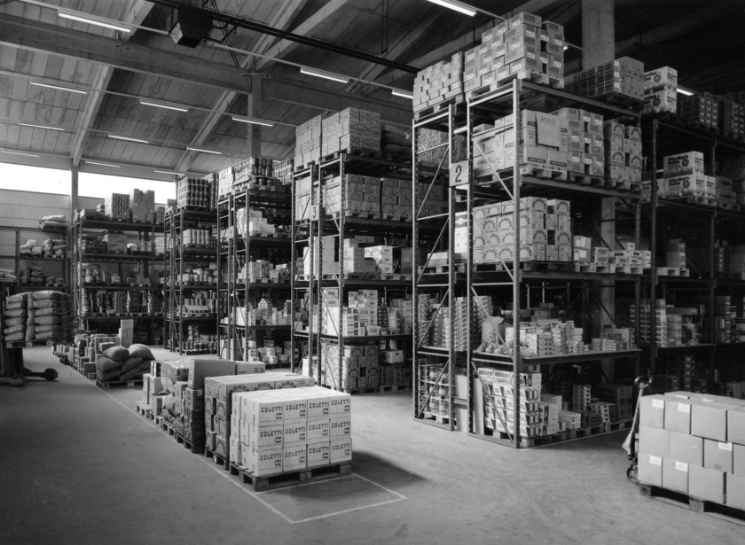 Schwarzweißfoto der großen Lagerhalle mit hohen Regalen voller Waren